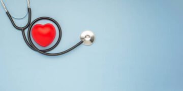 A stethoscope and red heart on a light blue background. Close-up photo. Top view. Flat lay. Space for text. Healthcare and medicine concept.