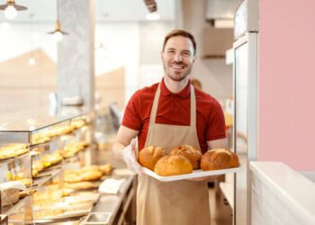Bakery shop owner with loaf of bred smiling to the camera while standing at pastry shop