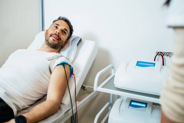 Handsome middle aged sporty man receiving modern physiotherapy treatment. Modern medicine concept.